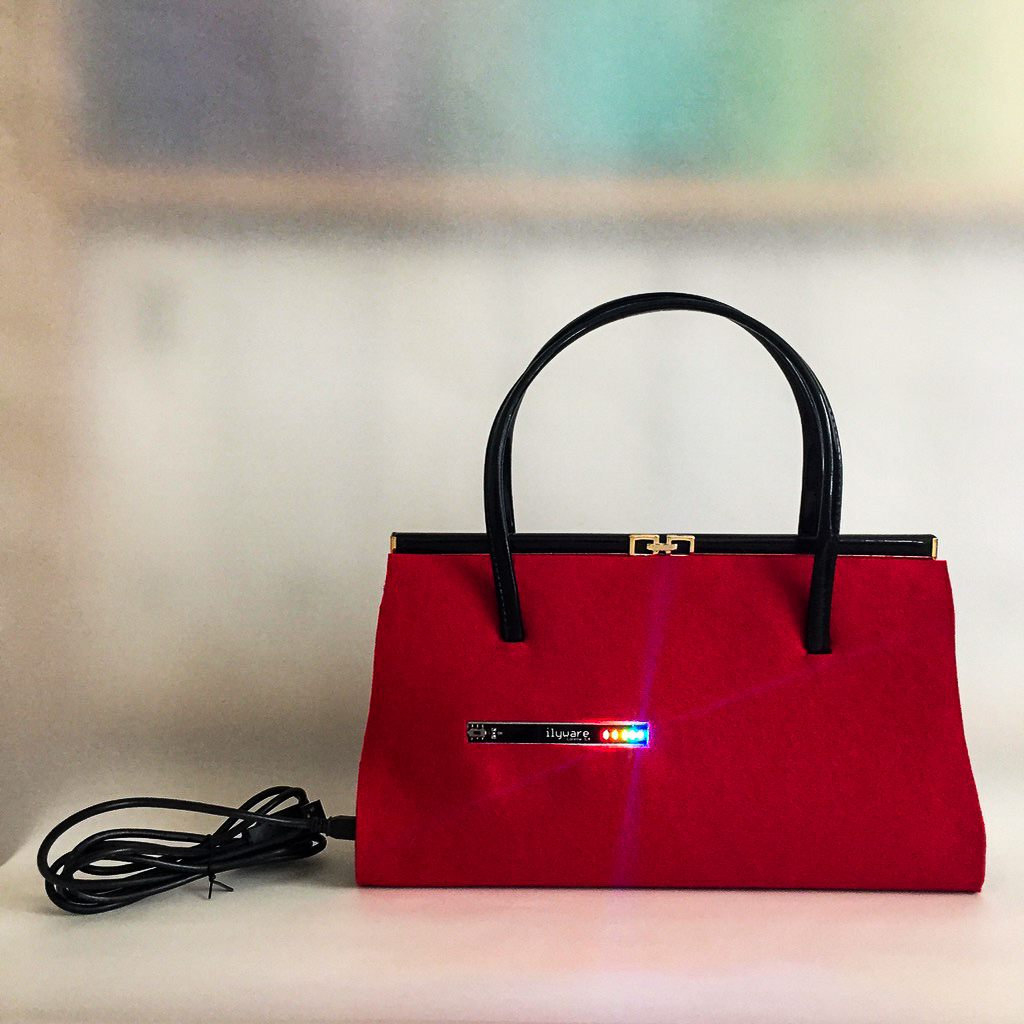 Red structured handbag centered in a clean studio setting, presented still to highlight its silhouette and texture against a minimal light background with a refined luxurious tone